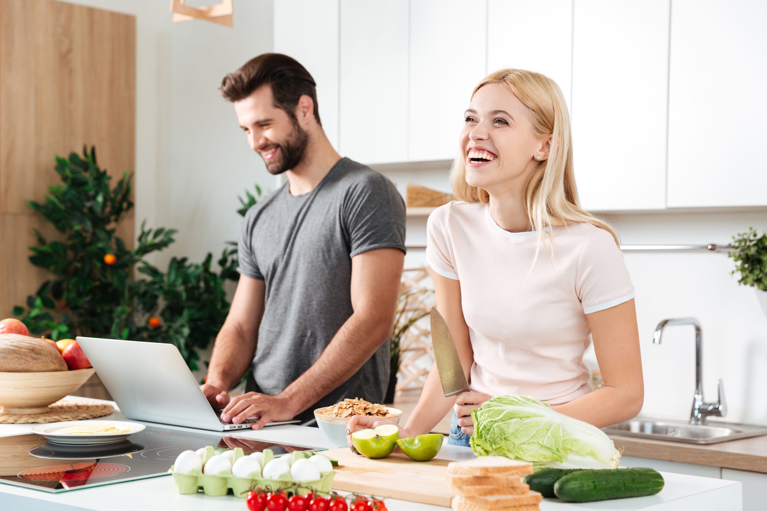 Smiling couple using notebook to cook in their kitchen and laughing